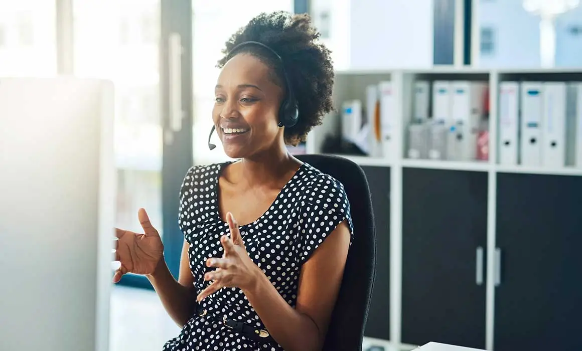 woman with headset smiling and talking into computer scren