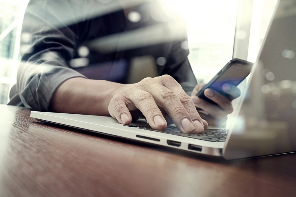 hand using laptop while other hand holds phone