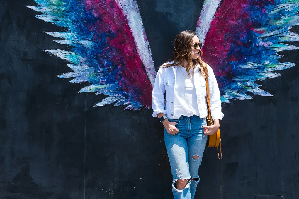 woman smiling and standing in front of wall with wings painted on it