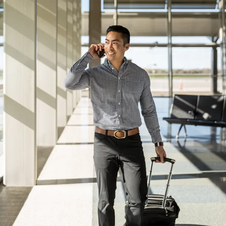 man with suitcase talking on phone while walking through an airport