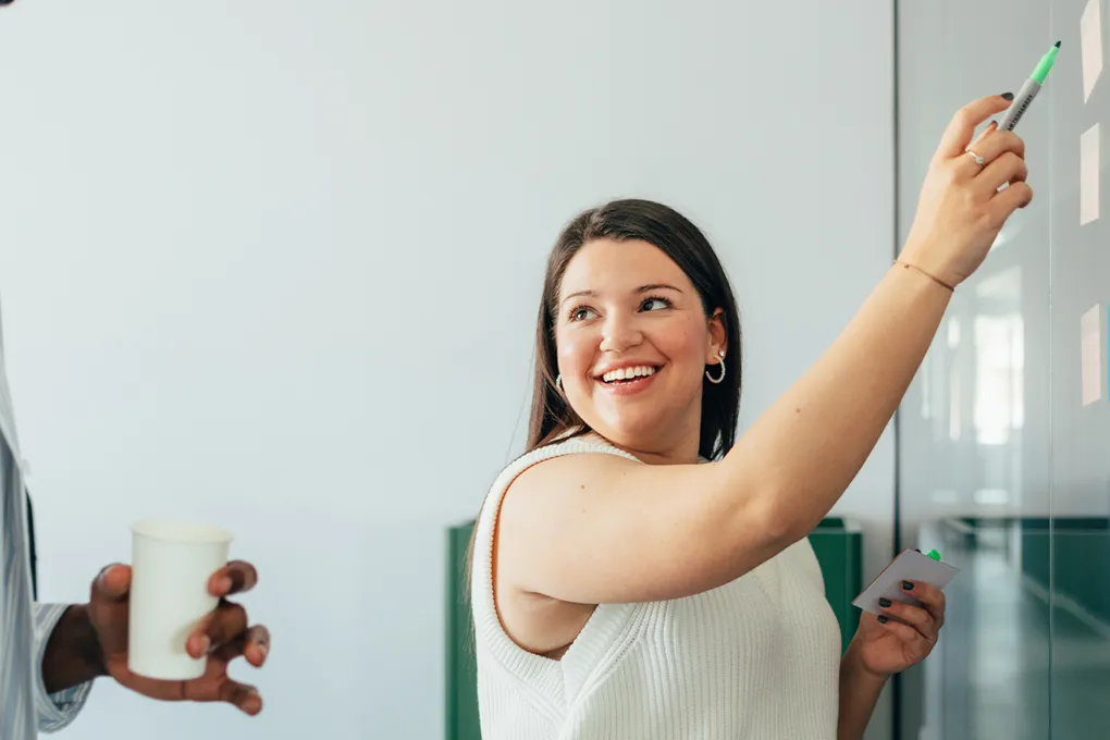 woman smiling and writing on white board